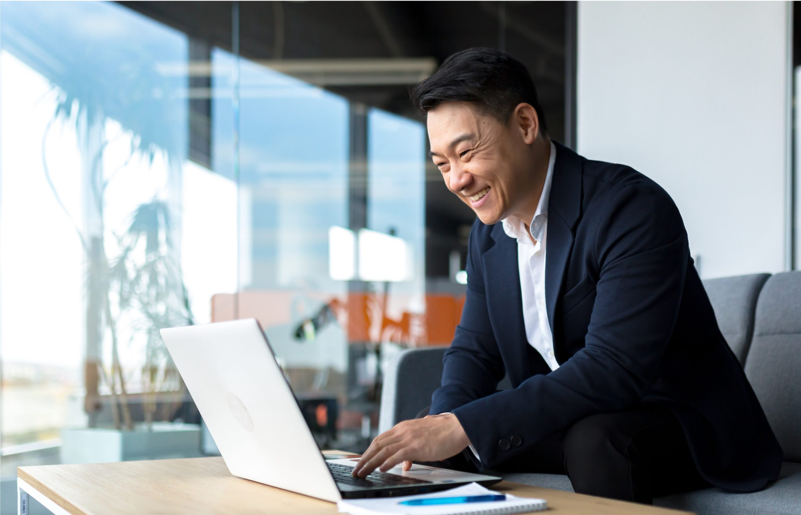 A successful California business owner and wealth management client happily works on his laptop in an office.