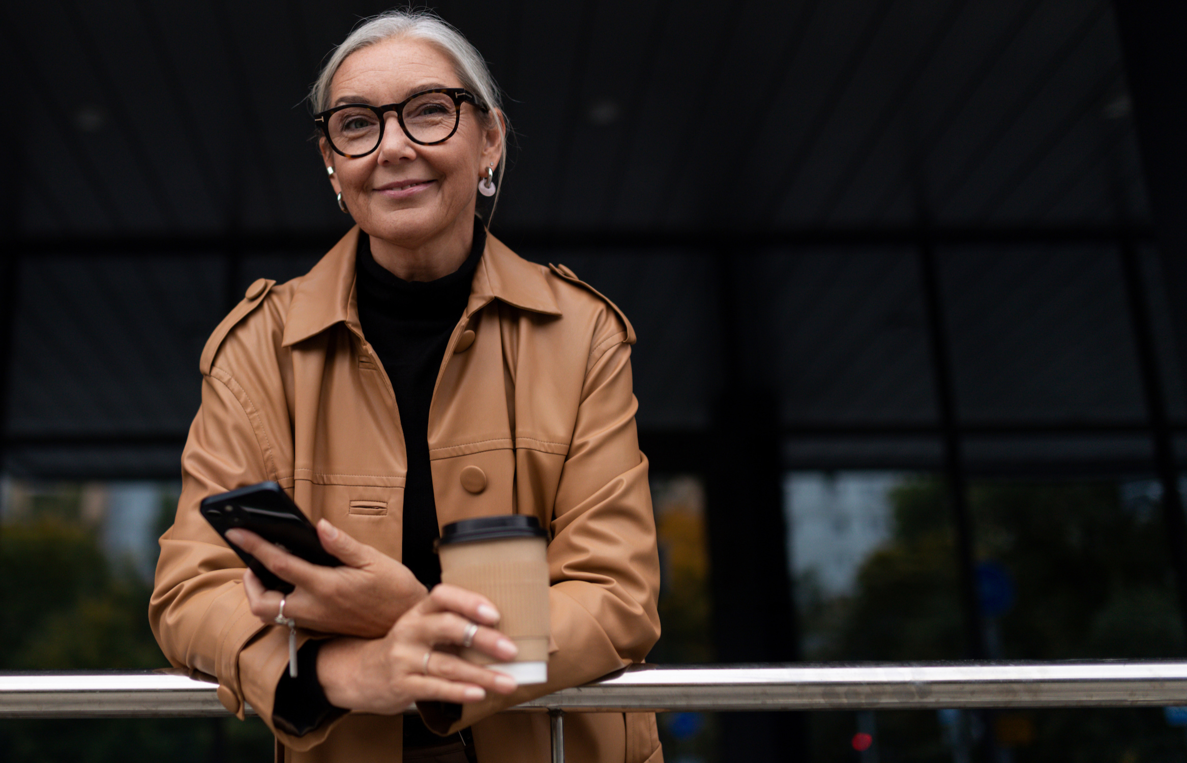 A high-net-worth retiree and wealth management client smiles, holding a cell phone and coffee cup.