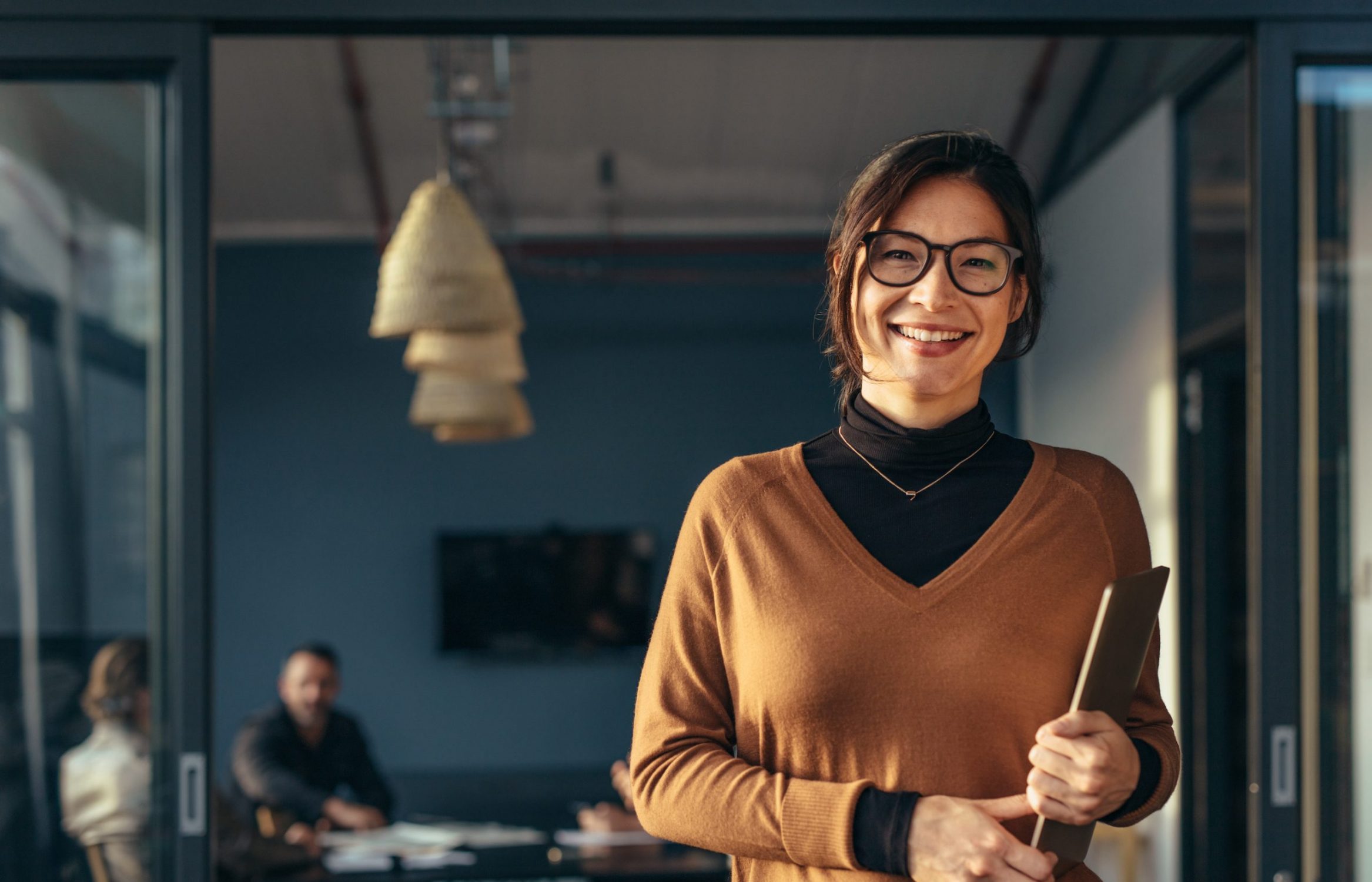 A financially independent woman and wealth management client smiles in front of an office meeting space.