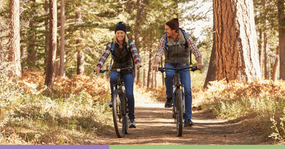 A middle-aged couple dressed for fall laugh as they ride bikes.